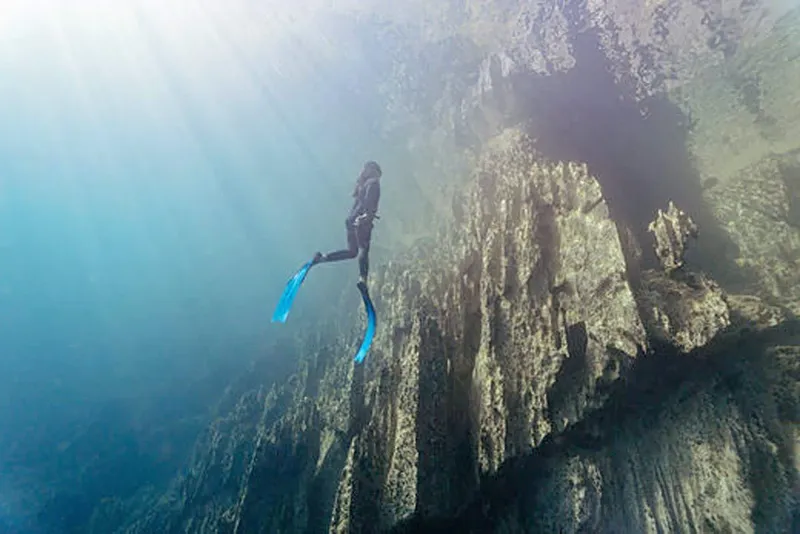 Apnea, une plongeuse explore une paroi rocheuse sous-marine lumineuse