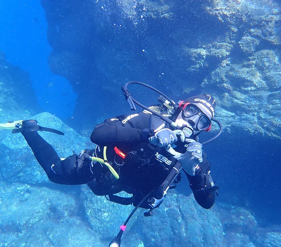 Plongeur en combinaison noire explore un récifal sous-marin bleu clair