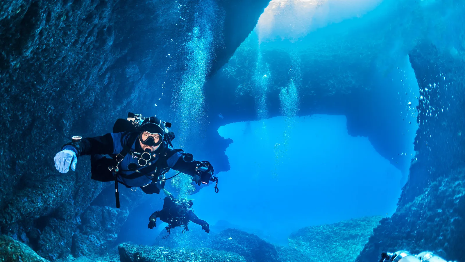 Deux plongeurs explorent une grotte sous-marine avec une lumière bleutée