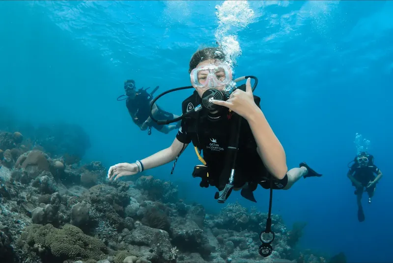 Trois plongeurs explorent un récifal corallien en eau turquoise