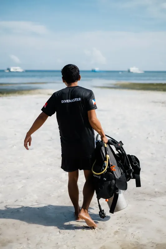Plongeur portant son équipement sur une plage de sable blanc