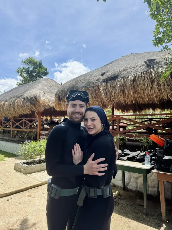 Couple souriant en combinaison de plongée devant une structure en chaume
