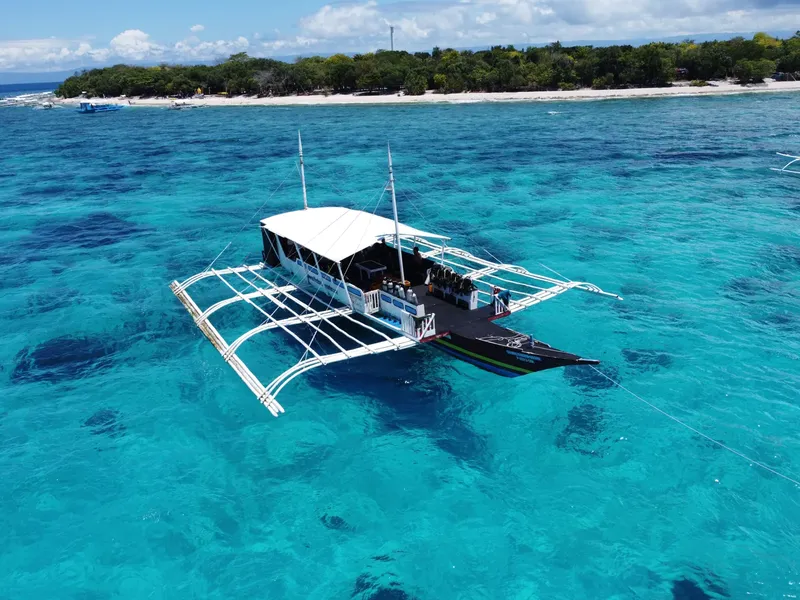 Bateau traditionnel philippin avec passagers sur une mer turquoise claire