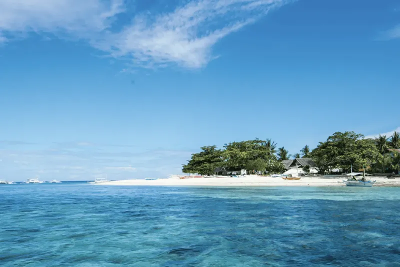 Plage de sable blanc avec quelques bateaux et végétation tropicale