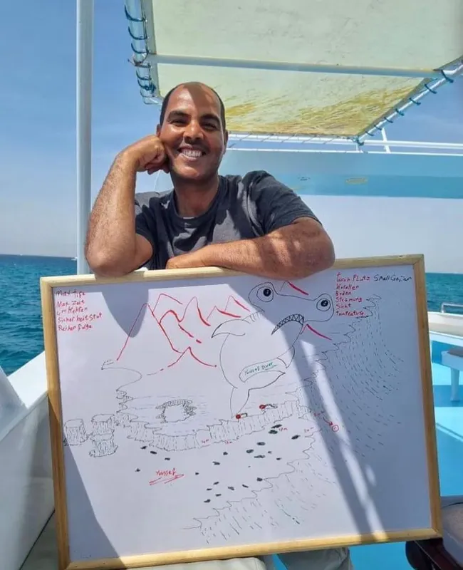Un homme souriant sur un bateau, tenant un tableau avec un dessin de poisson