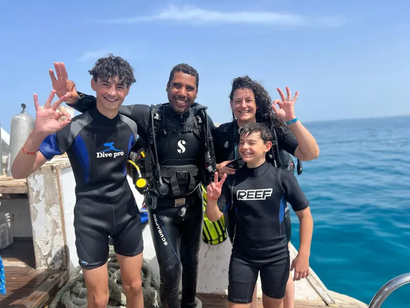 Quatre personnes souriantes en combinaison de plongée sur un bateau