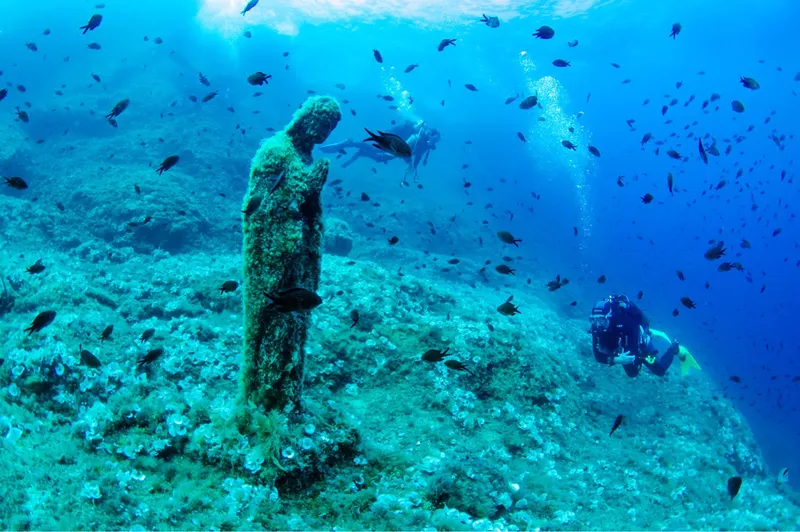 Plongée sous-marine avec statue coloniale et banc de poissons