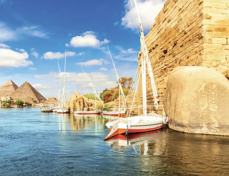 Voiliers amarrés sur un fleuve avec pyramides en arrière-plan