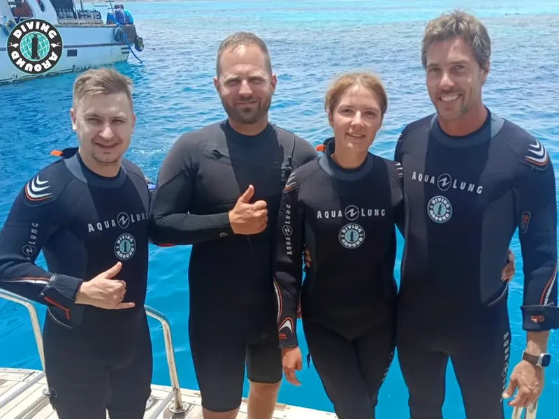 Quatre plongeurs souriants en combinaison sur un ponton ensoleillé