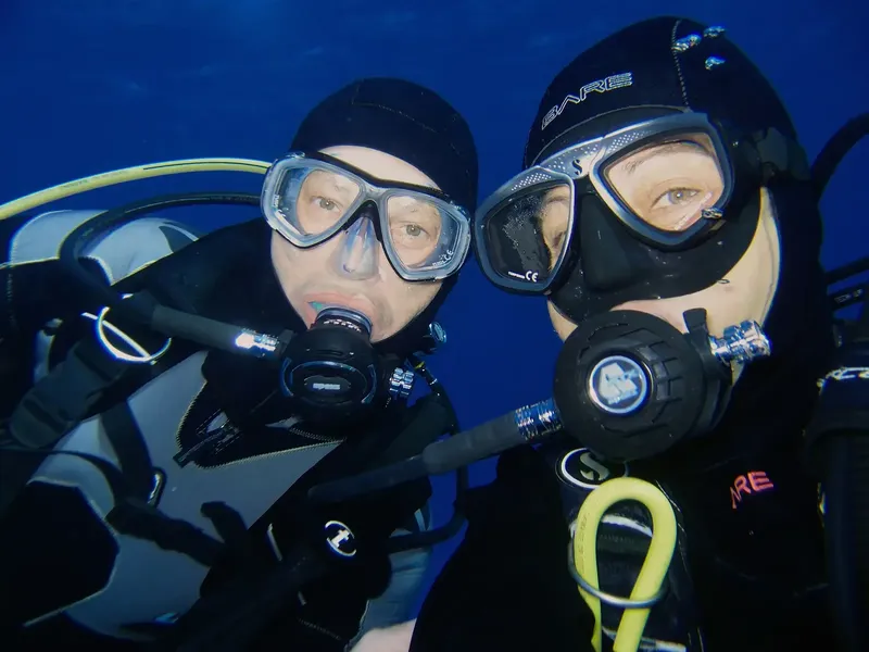Deux plongeurs en combinaison regardent vers l'appareil photo sous l'eau