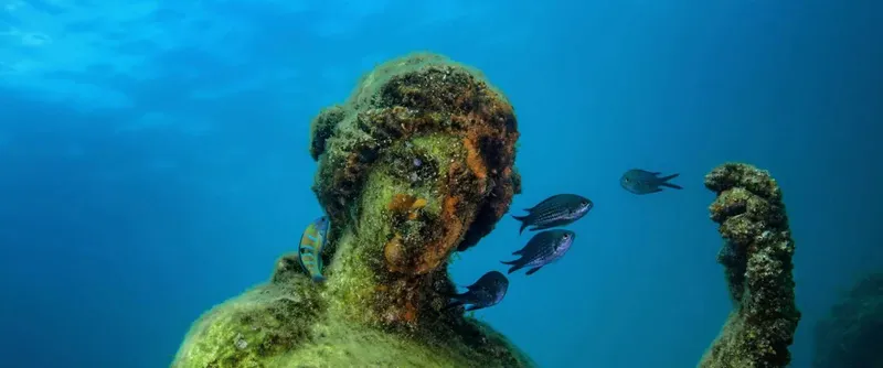 Statue antique submergée, entourée de petits poissons bleus dans l'eau
