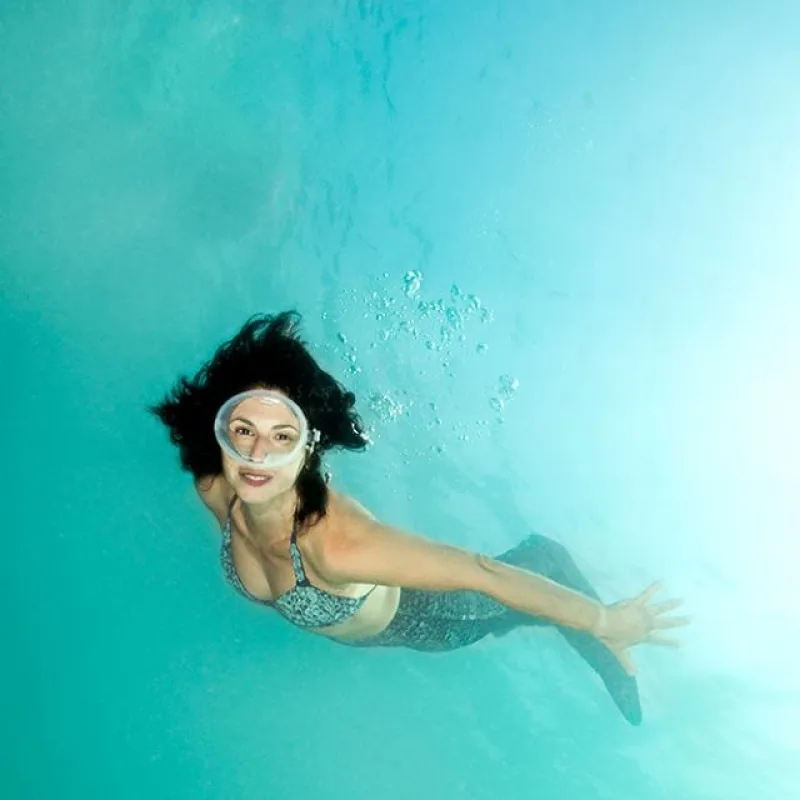 Femme souriante nageant en apnée dans une eau turquoise claire