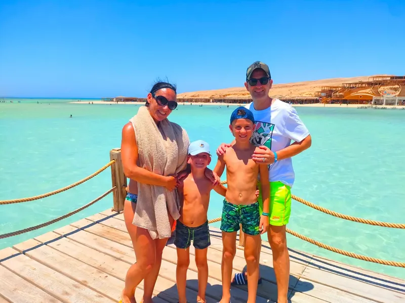 Famille souriante sur un ponton en bois au bord de l'eau turquoise