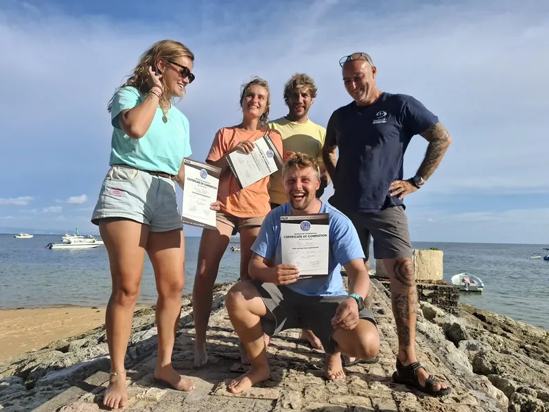 Groupe de plongeurs souriants tenant des certificats de formation en bord de mer