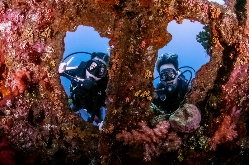 Deux plongeurs explorent une ouverture dans un récif corallien coloré