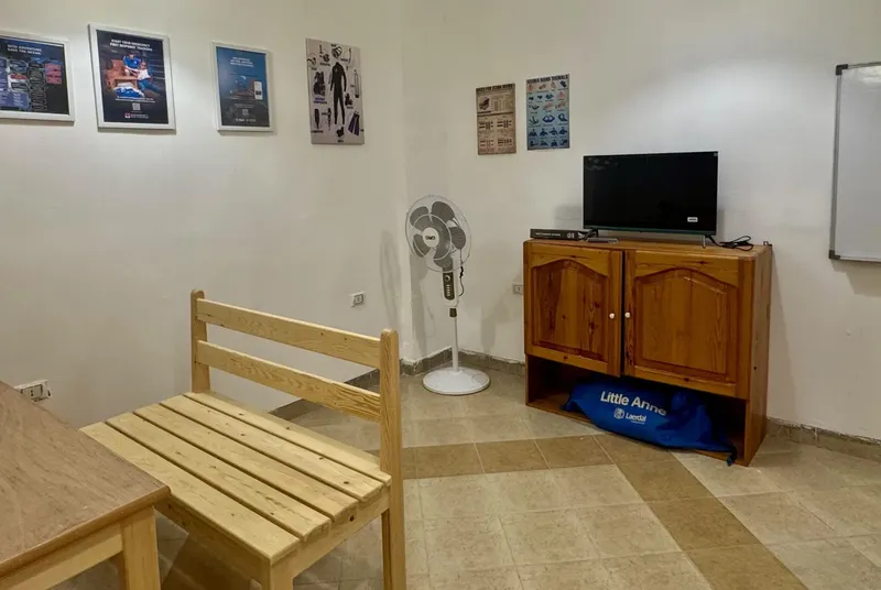 Salle de cours avec banc en bois, ventilateur et meuble TV