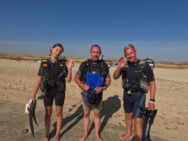 Trois plongeurs souriants sur une plage de sable avec leur équipement