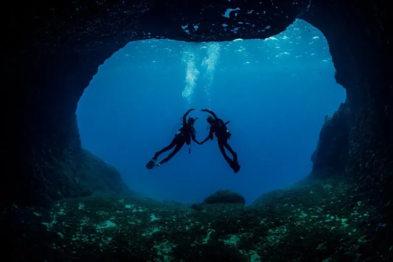 Deux plongeurs explorent une grotte sous-marine, lumière bleue, bulles