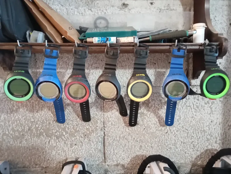 Ordinateurs de plongée colorés accrochés à une étagère en bois