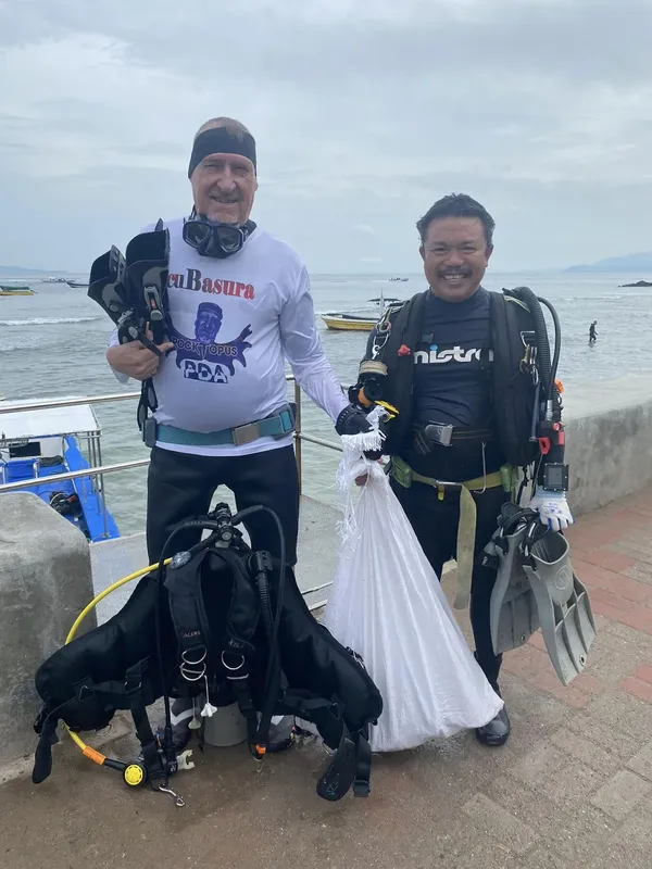 Deux plongeurs équipés posent devant un quai et la mer
