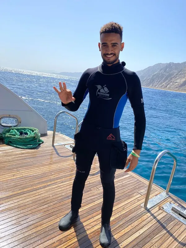 Plongeur souriant en combinaison, faisant un signe de la main sur un bateau