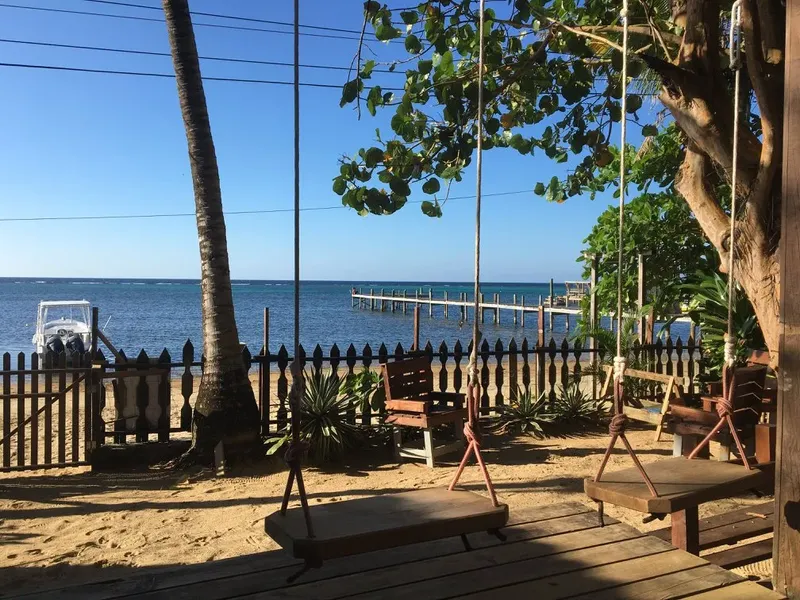 Plage de sable, bateaux amarrés, balançoires en bois et végétation tropicale