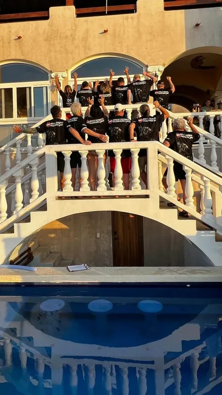 Groupe de personnes souriantes sur un balcon avec un escalier et piscine