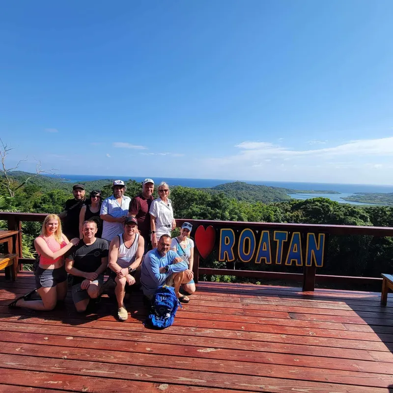 Groupe de personnes souriantes posant devant un paysage tropical et un panneau