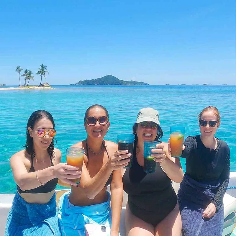Quatre femmes souriantes trinquent sur un bateau en mer turquoise