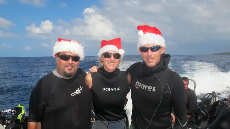Trois plongeurs souriants portant des bonnets de Père Noël en mer