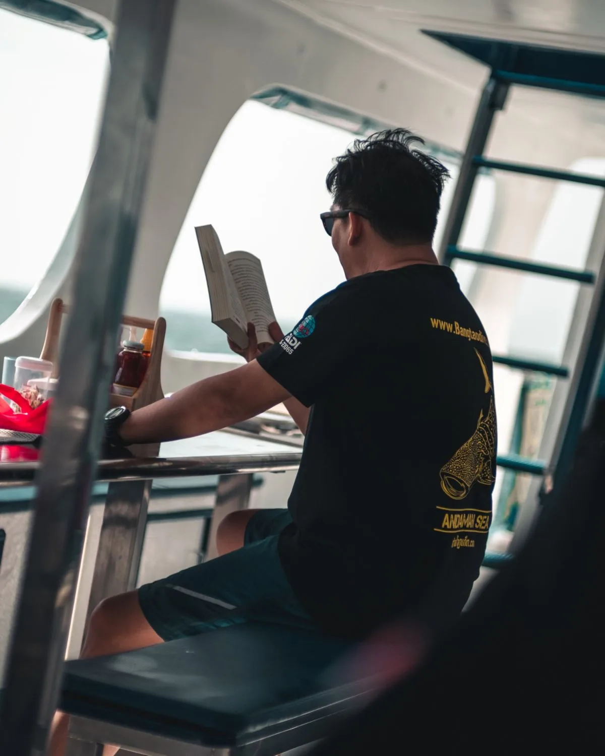 Homme lisant un livre sur le pont d'un bateau en mer