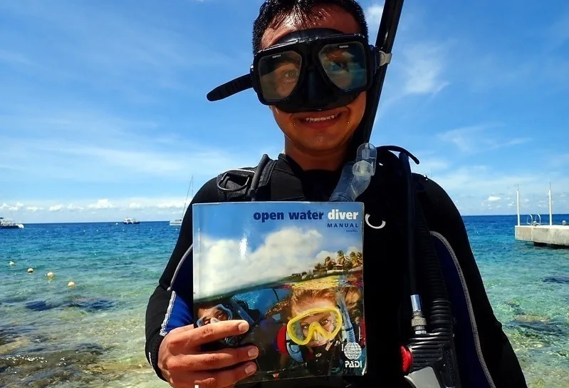 Plongeur souriant tenant un manuel PADI avec équipement de plongée