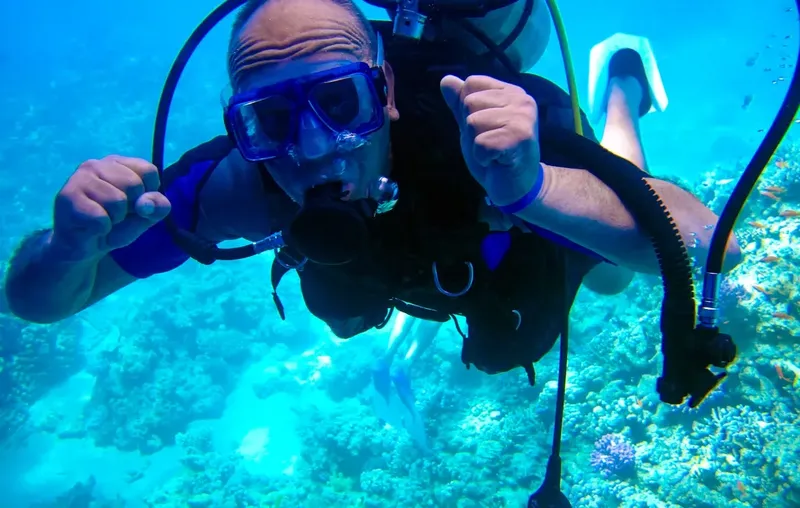 Plongeur souriant avec signe OK, corail et poissons en arrière-plan