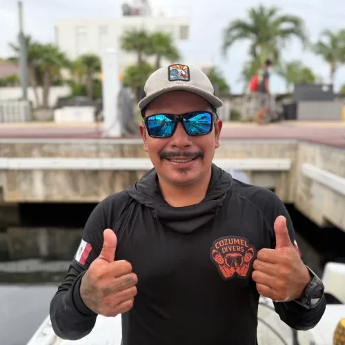 Homme souriant avec lunettes de soleil et casquette faisant un signe de pouce levé