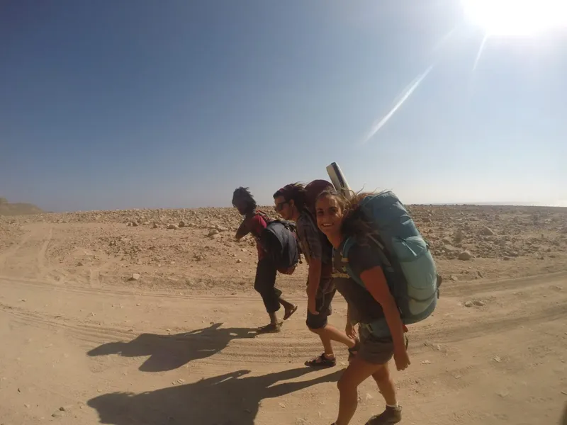 Trois personnes marchent avec des sacs à dos dans un paysage désertique ensoleillé