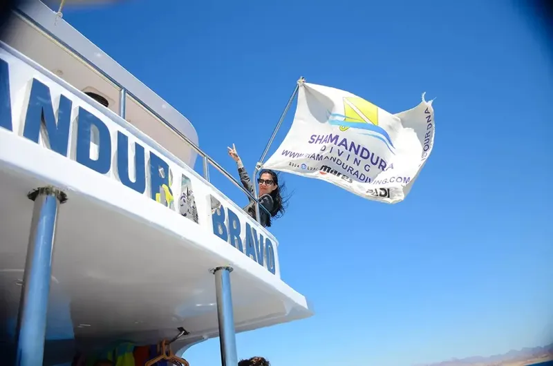 Femme souriante sur un bateau de plongée avec un drapeau agité