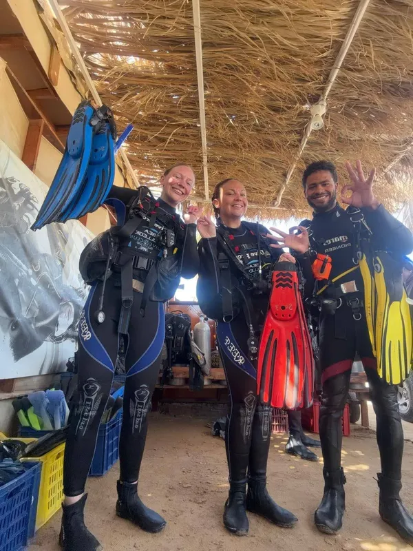 Trois plongeurs souriants équipés prêts pour une immersion en mer
