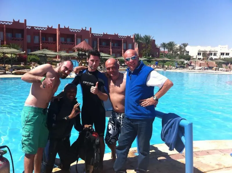 Quatre hommes et une femme souriants près d'une piscine avec équipement