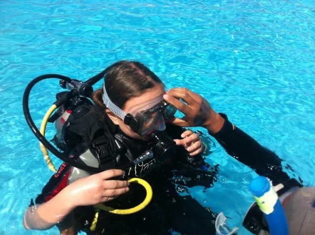 Une plongeuse en formation se fait ajuster son masque dans une piscine
