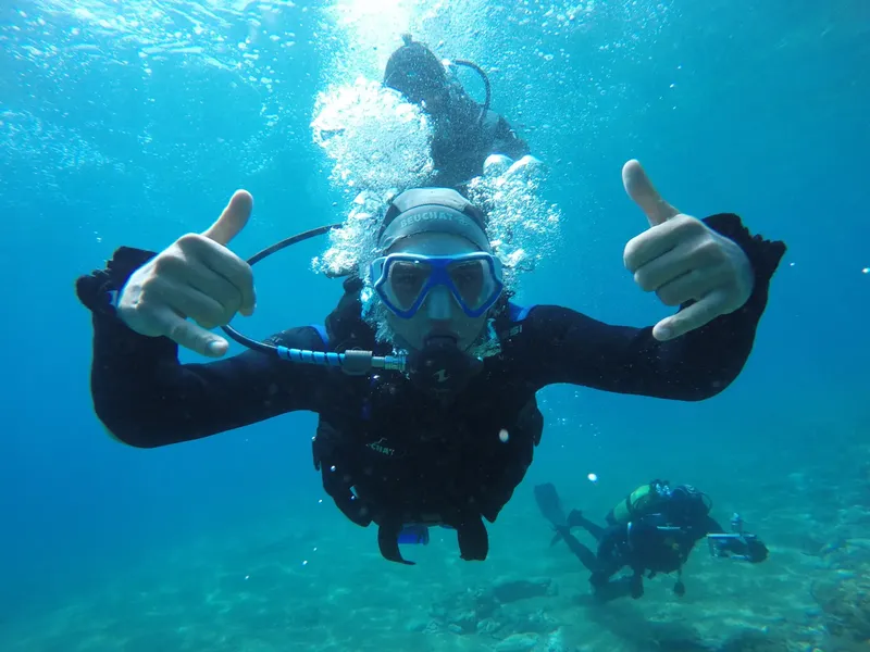 Plongeur souriant avec pouces levés sous l'eau, ambiance claire et bleue