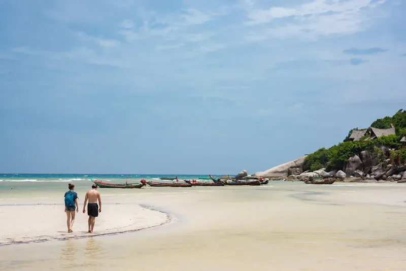 Deux personnes marchent sur une plage tropicale avec des bateaux