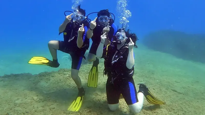 Trois plongeurs souriants font des signes de la main sous l'eau