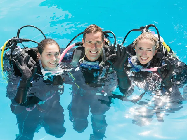 Trois plongeurs souriants avec leur équipement dans l'eau turquoise