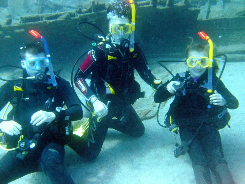 Trois plongeurs en équipement complet posent sous l'eau dans un bassin