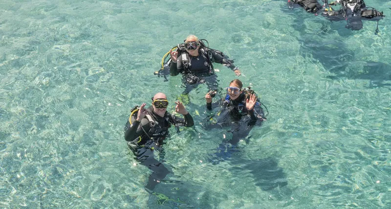 Trois plongeurs souriants et équipés dans une eau turquoise claire