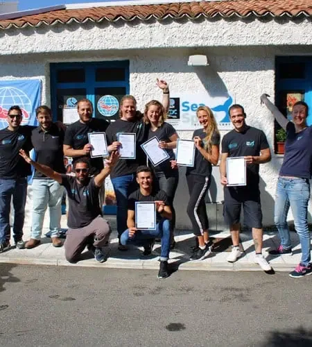 Groupe de plongeurs souriants tenant leurs certificats devant un bâtiment