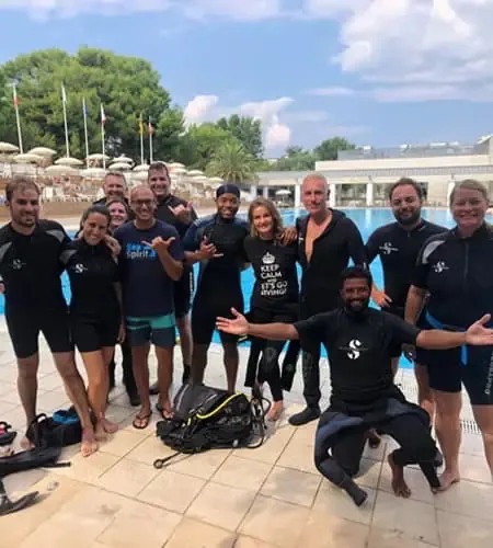 Groupe de plongeurs souriants posant devant une piscine ensoleillée