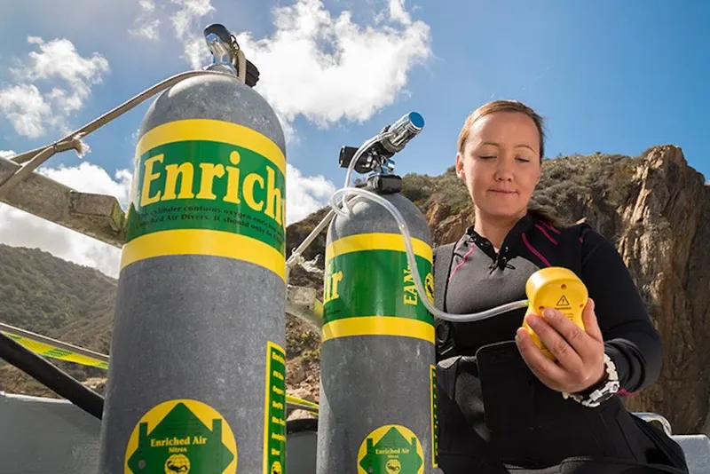 Plongeuse vérifiant un analyseur d'air devant des bouteilles enrichies en oxygène