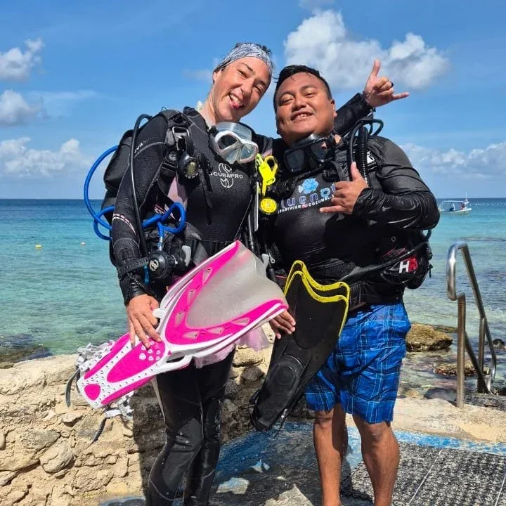 Deux plongeurs souriants équipés près d'une plage ensoleillée