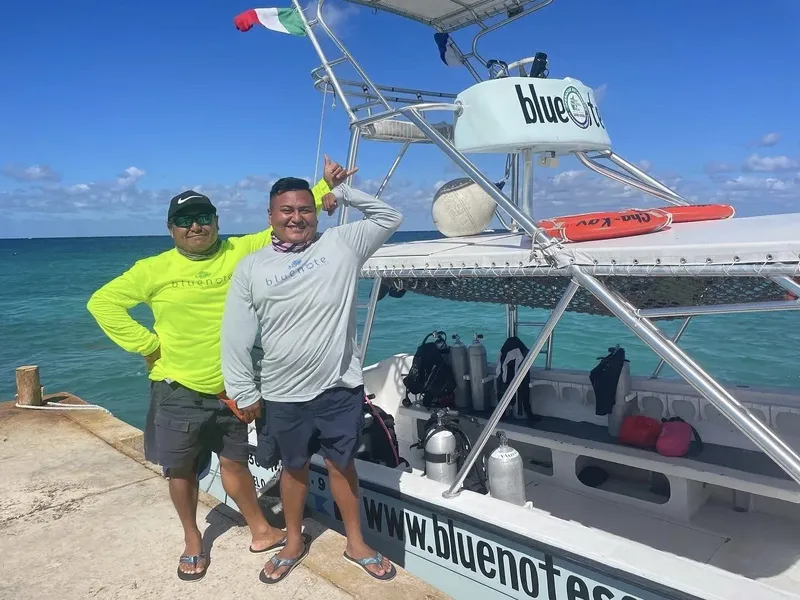 Deux hommes souriants posent devant un bateau de plongée bleu et blanc